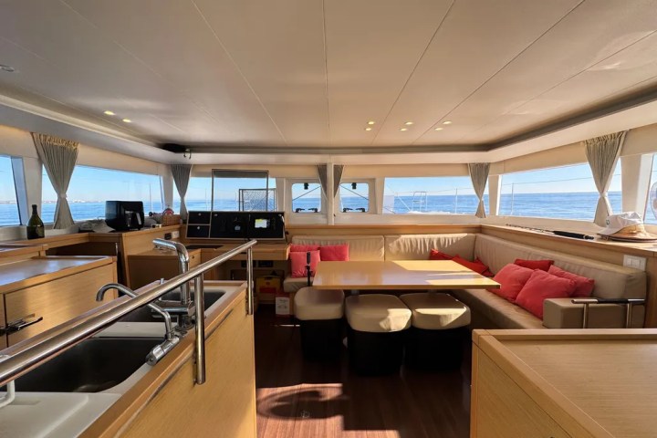 Luxurious yacht interior with a table, beige seating, and large windows showing the ocean view.