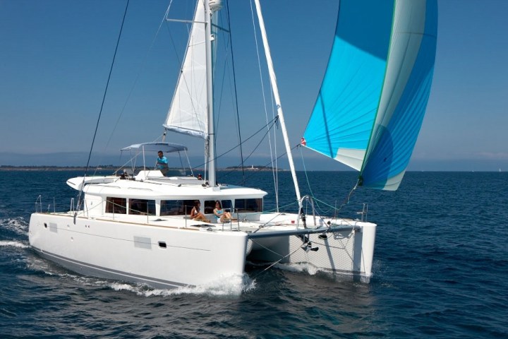 A white catamaran sailing with blue sails on a clear, sunny day.