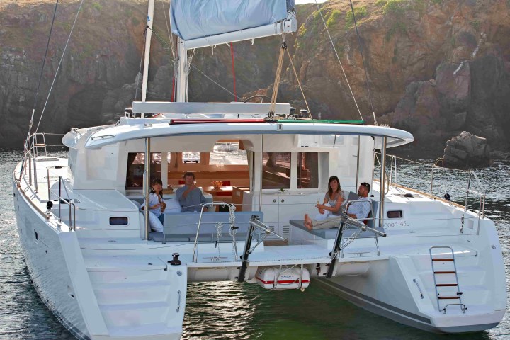 Four people relaxing on a white catamaran near rocky cliffs.