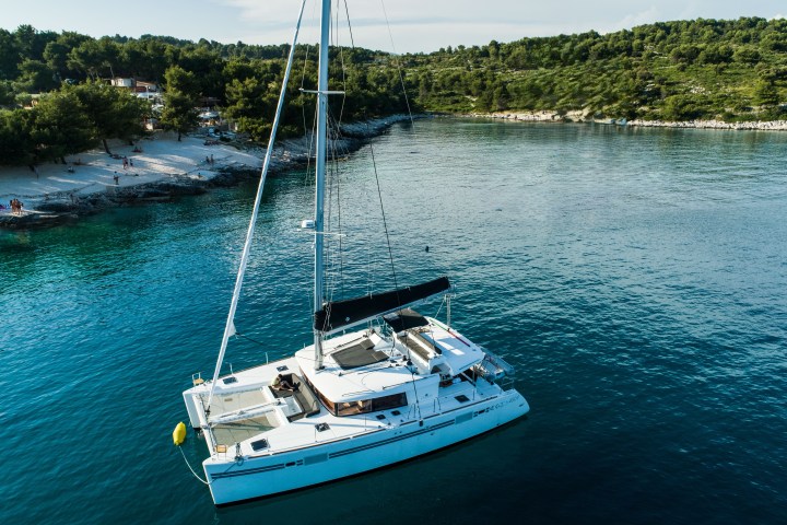 White catamaran anchored near a wooded shoreline on a sunny day.