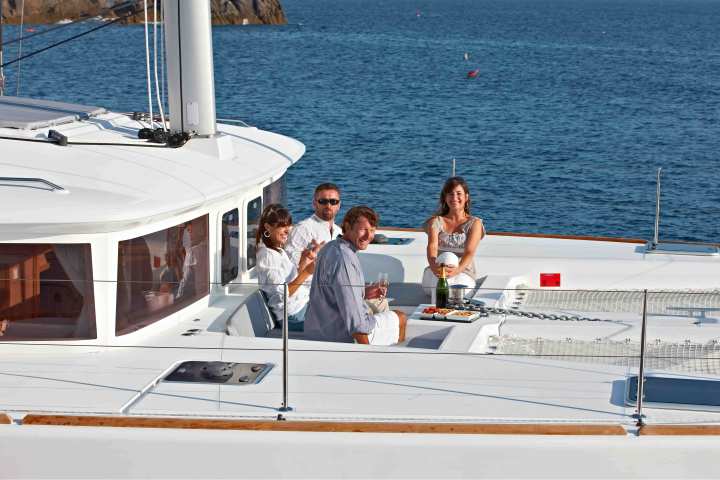 Four people relaxing and dining on a white yacht with a blue ocean in the background.
