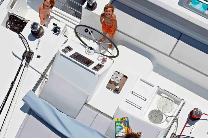Overhead view of three people on a white boat deck; two children near the helm, one person sunbathing.