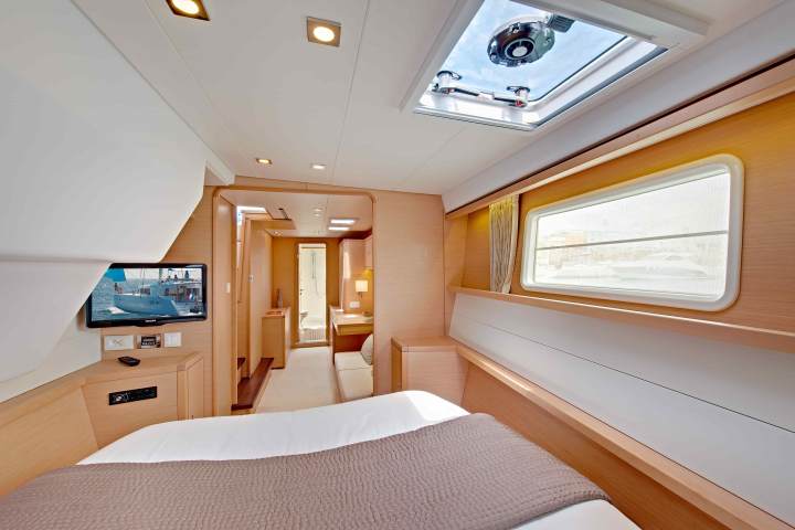 Modern yacht bedroom with bed, TV, window, and skylight, leading to bathroom.