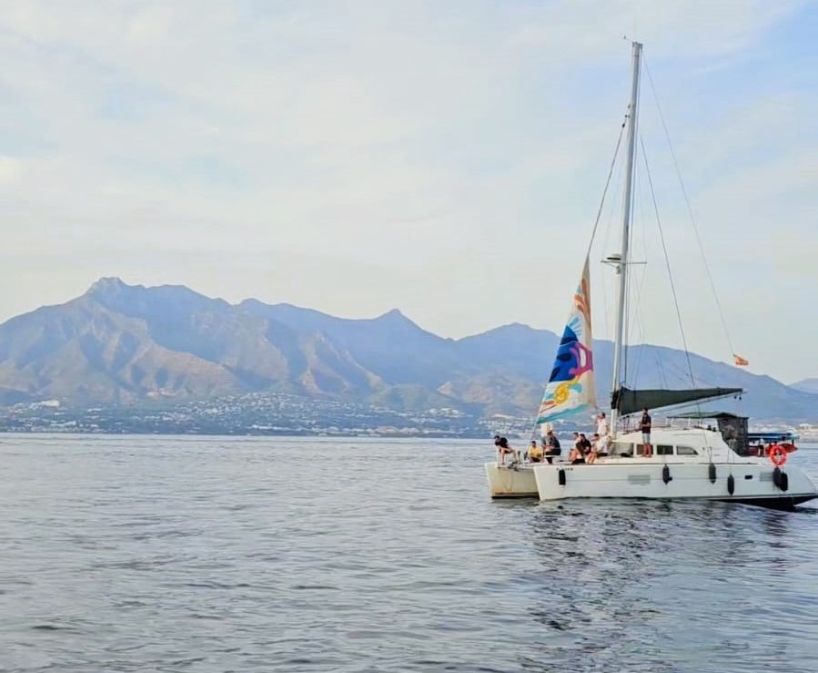 2025-09-24 Catamaran with colorful sail on calm water, mountains in background.