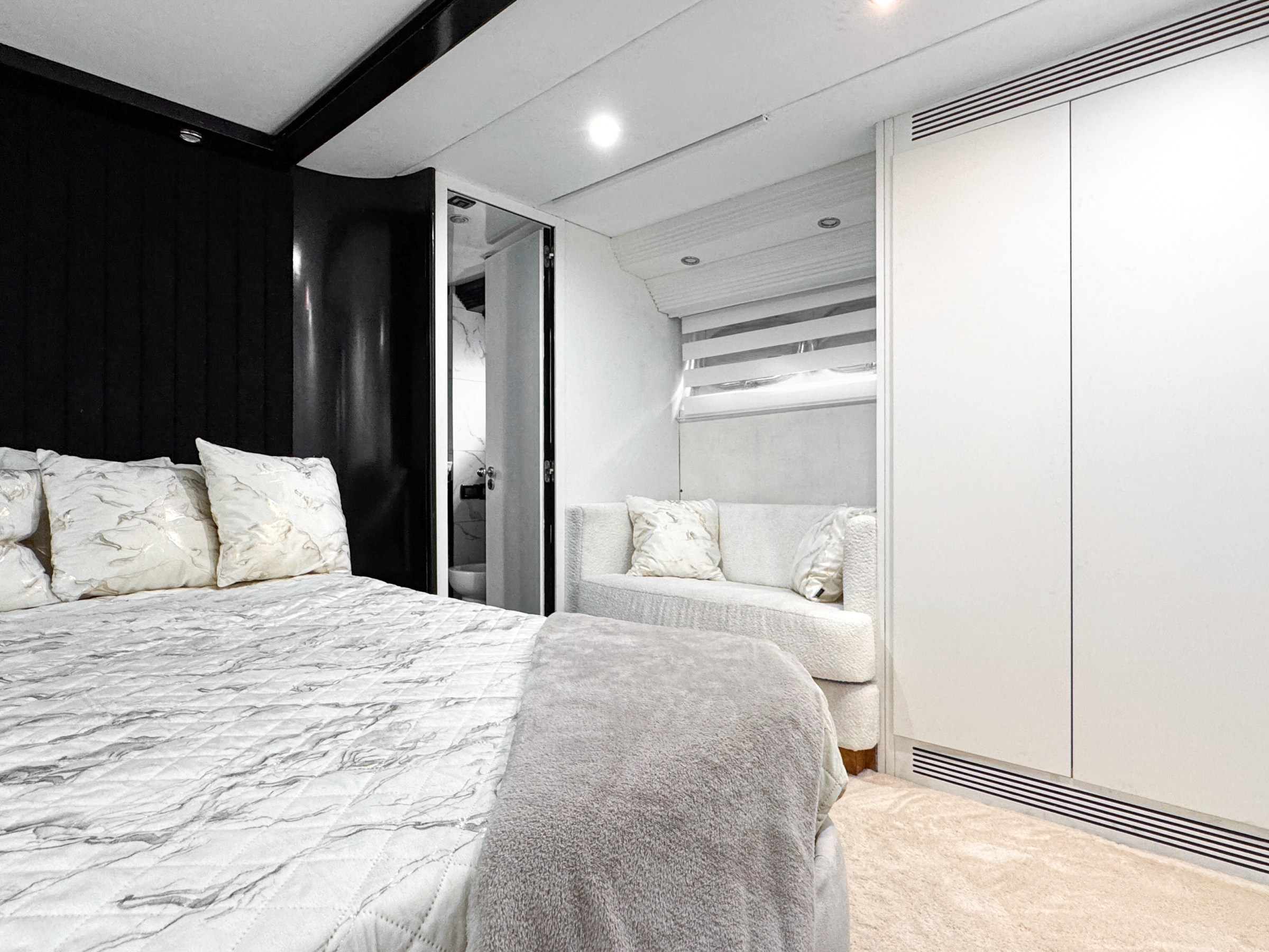 Modern bedroom with bed, pillows, sofa, white closet, and open door.