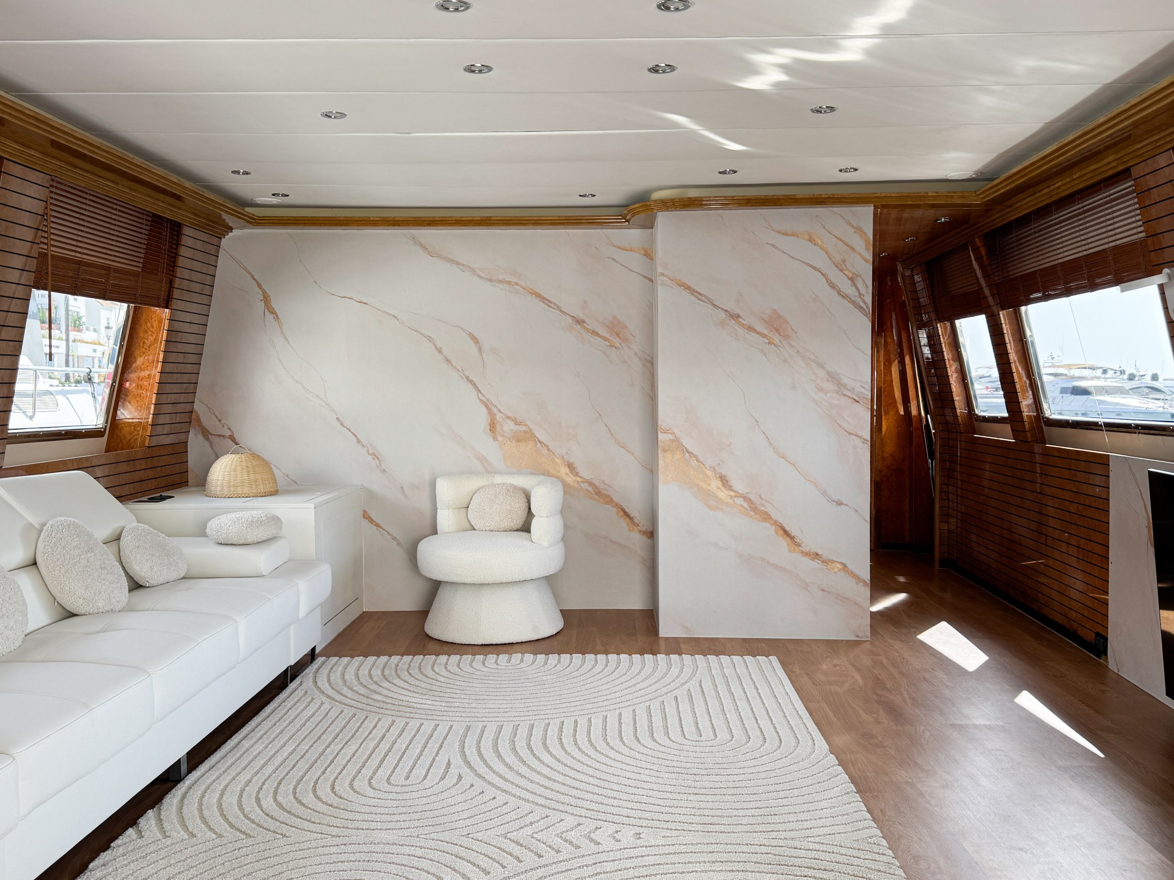 Luxurious yacht interior with white sofa, round chair, marble wall, and large windows.