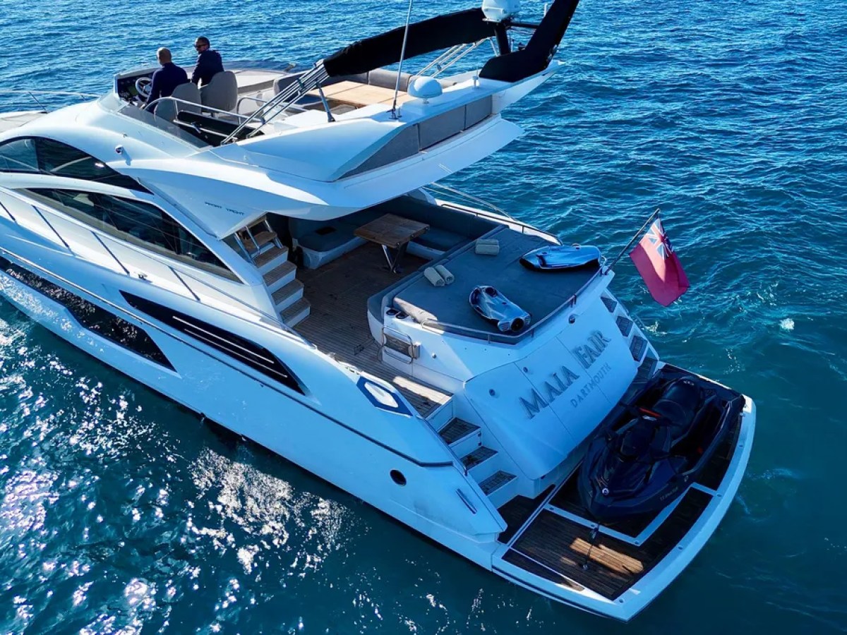 A luxury yacht with two people navigating, sailing on clear blue water.