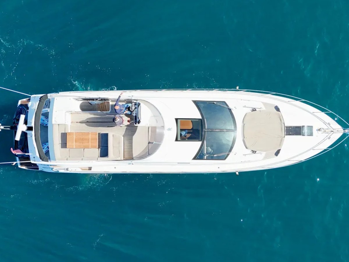 Aerial view of a white yacht on a blue sea, with people on deck.