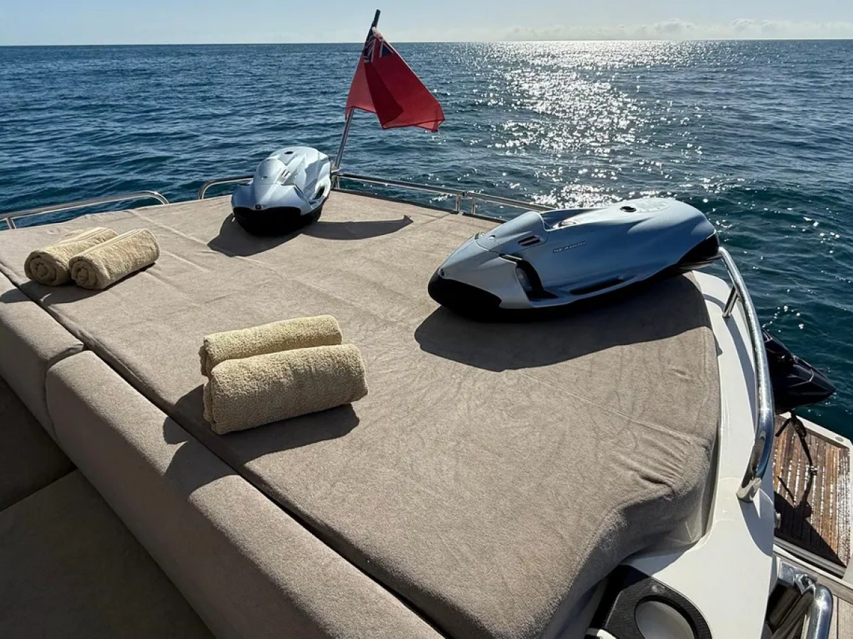 Boat deck with two sea scooters, three rolled towels, and a red flag against the ocean.
