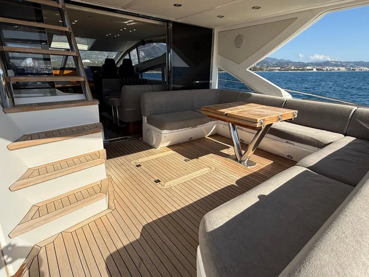 Luxury yacht deck with sectional sofa, wooden table, stairs, and sea view.
