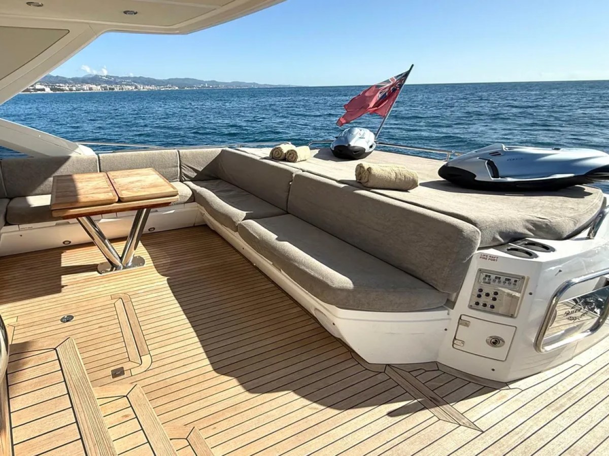 Luxury yacht deck with sofa, wooden table, and ocean view with blue sky.