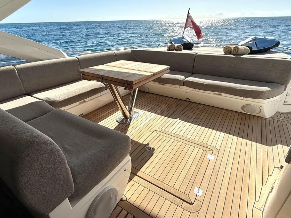 Outdoor yacht deck with wooden table, gray sofas, and ocean view.