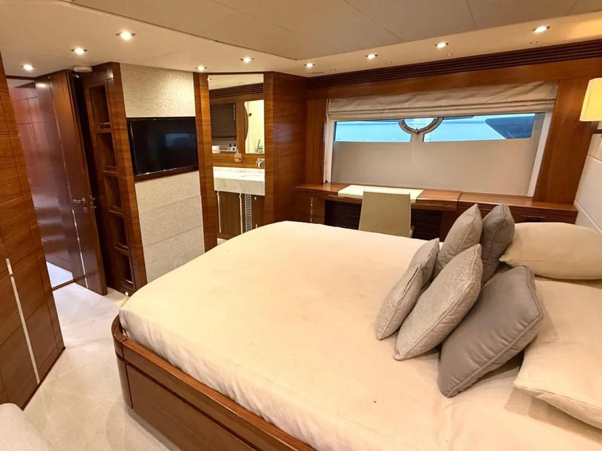 Luxurious yacht bedroom with bed, pillows, TV, vanity desk, and window view.