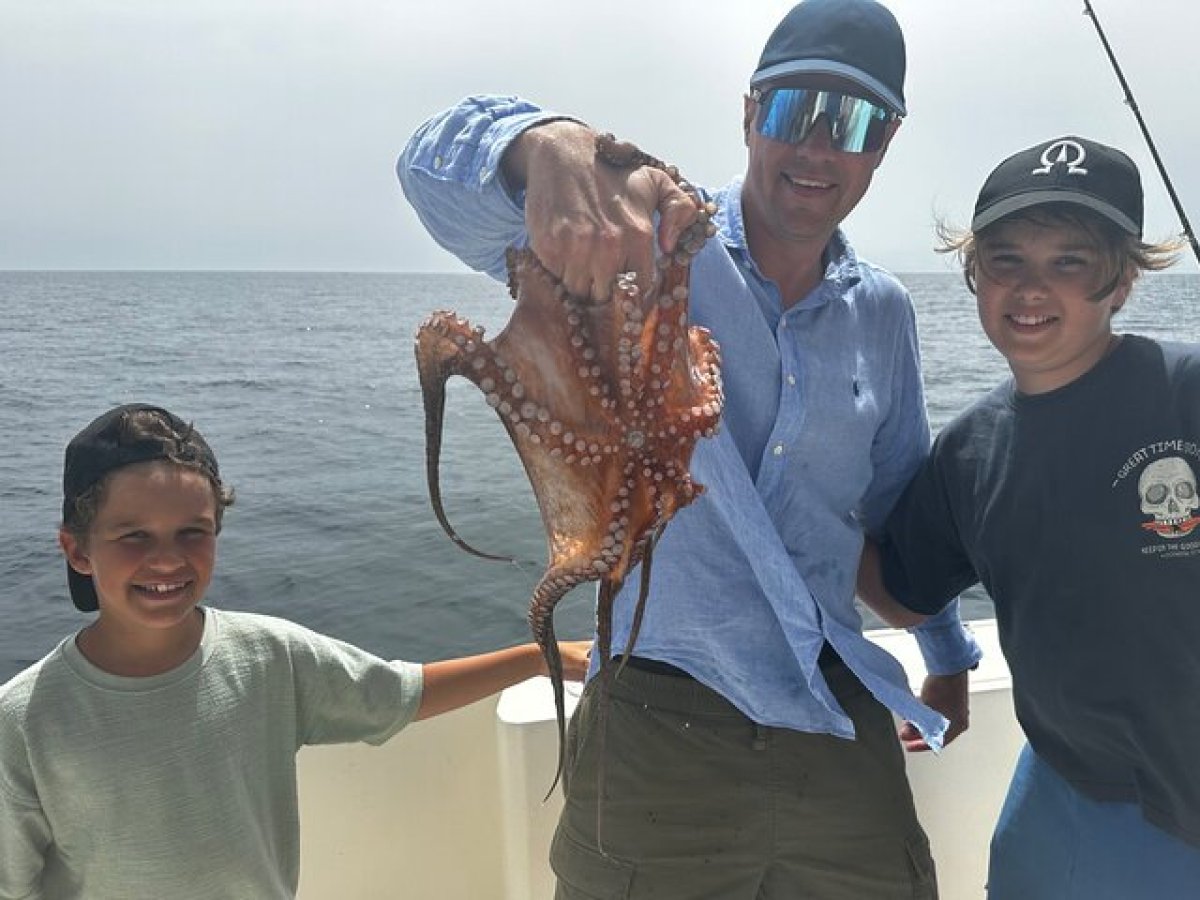 Three people on a boat holding a caught octopus.