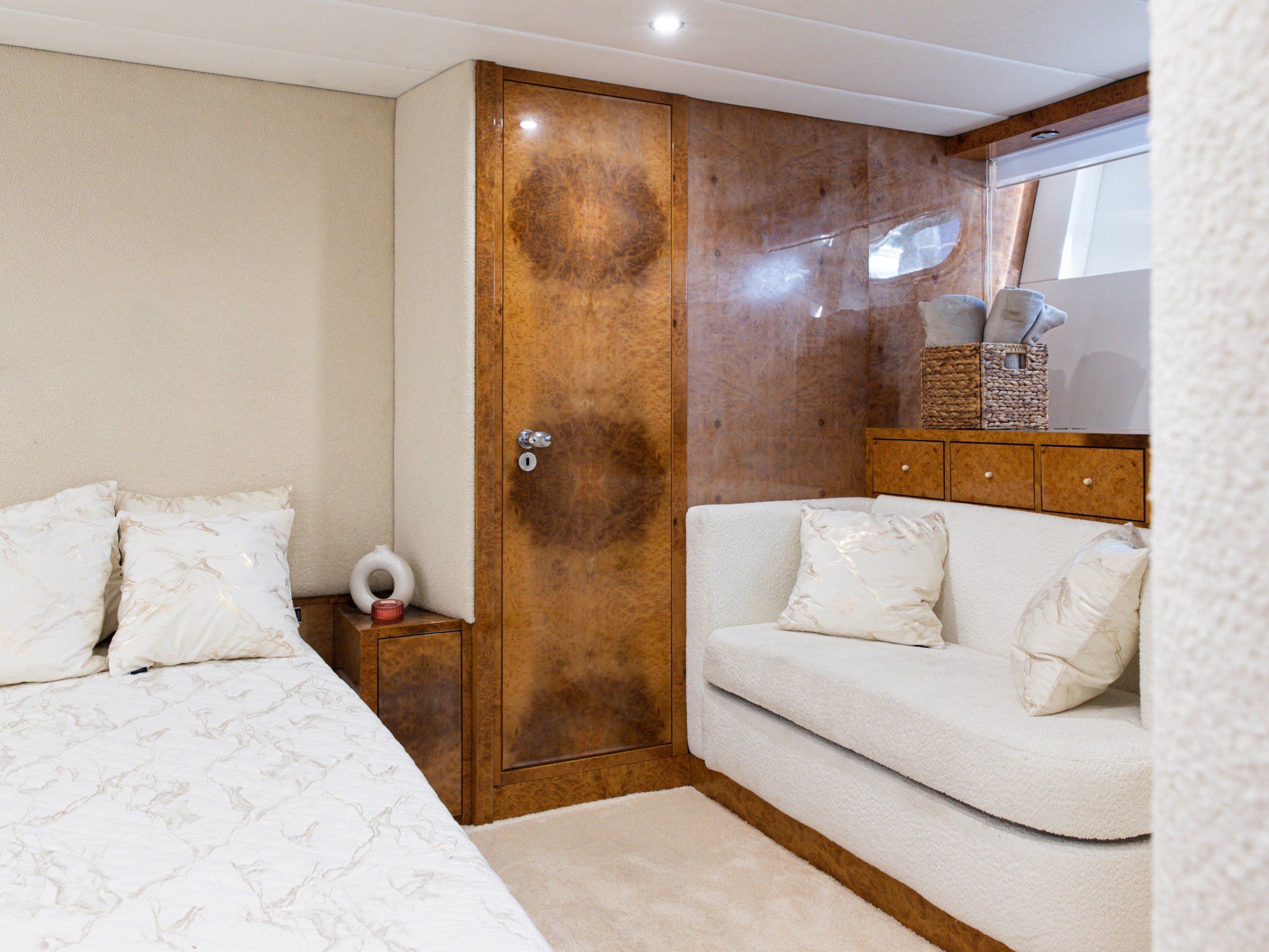 Cozy yacht cabin with bed, wood details, sofa, and wicker baskets on a shelf.