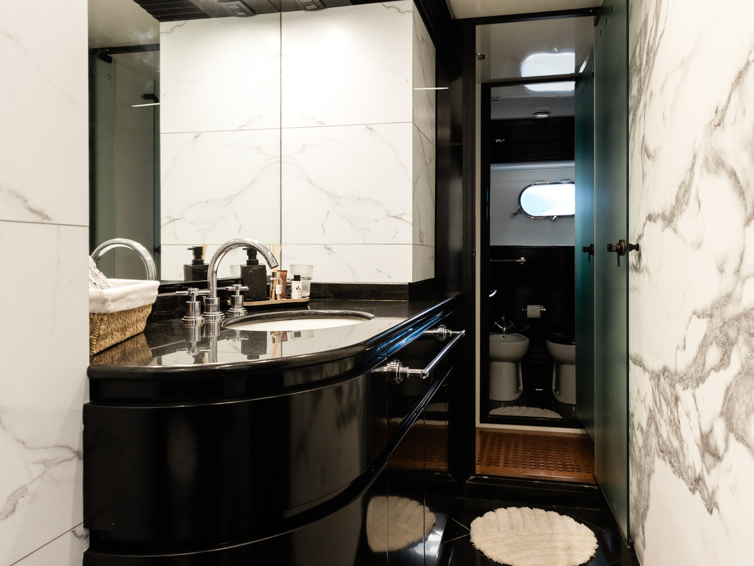Luxurious bathroom with marble walls, black vanity, and a peek into a toilet area with frosted glass door.