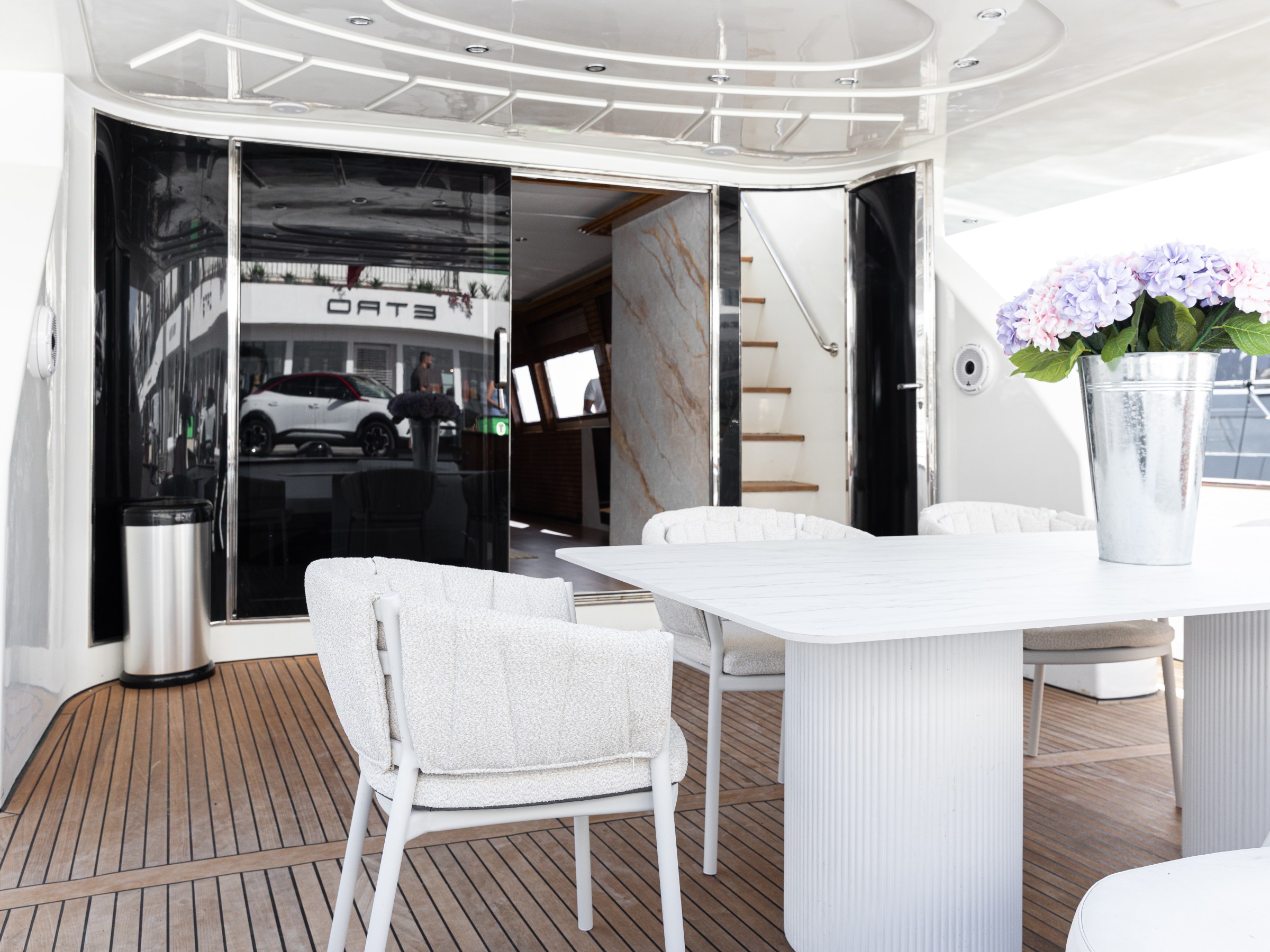 Luxury yacht deck with table, chairs, and flower vase under a covered area.