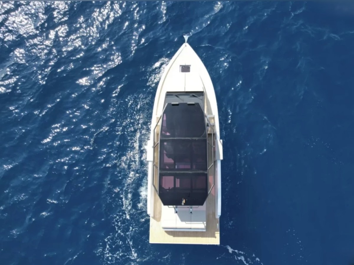 Aerial view of a white boat with a glass roof on blue ocean water.