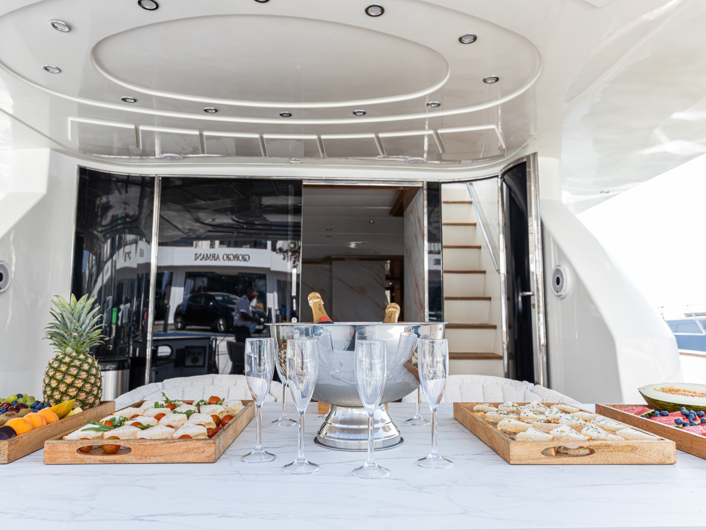 Table on a yacht with fruit platters, sandwiches, and champagne glasses.
