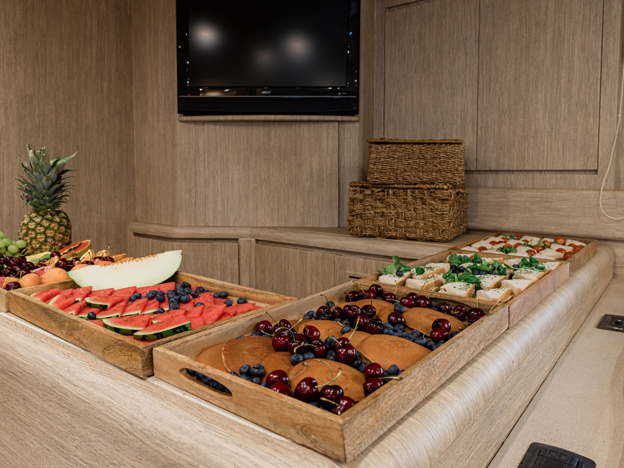 Trays of assorted fruits and sandwiches on a wooden counter.