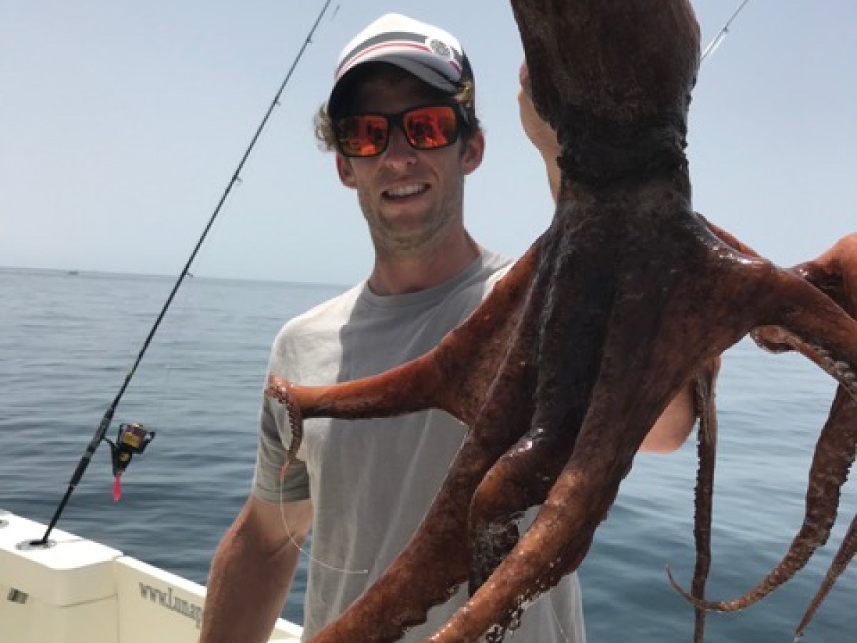 Person holding a large octopus on a boat with fishing gear.