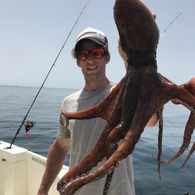 Person holding a large octopus on a boat with fishing gear.