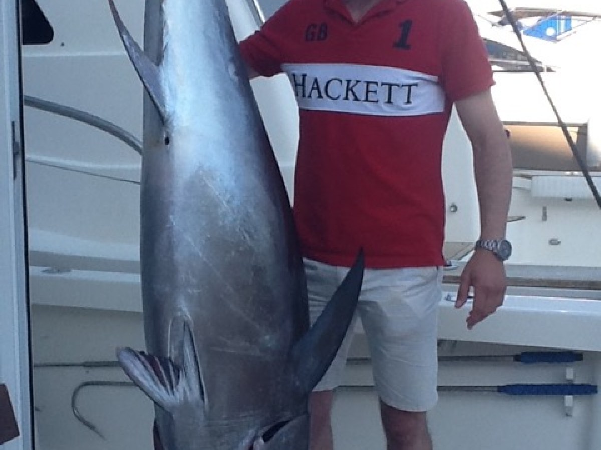 Man in red shirt posing with large fish on a boat.
