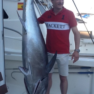 Man in red shirt posing with large fish on a boat.