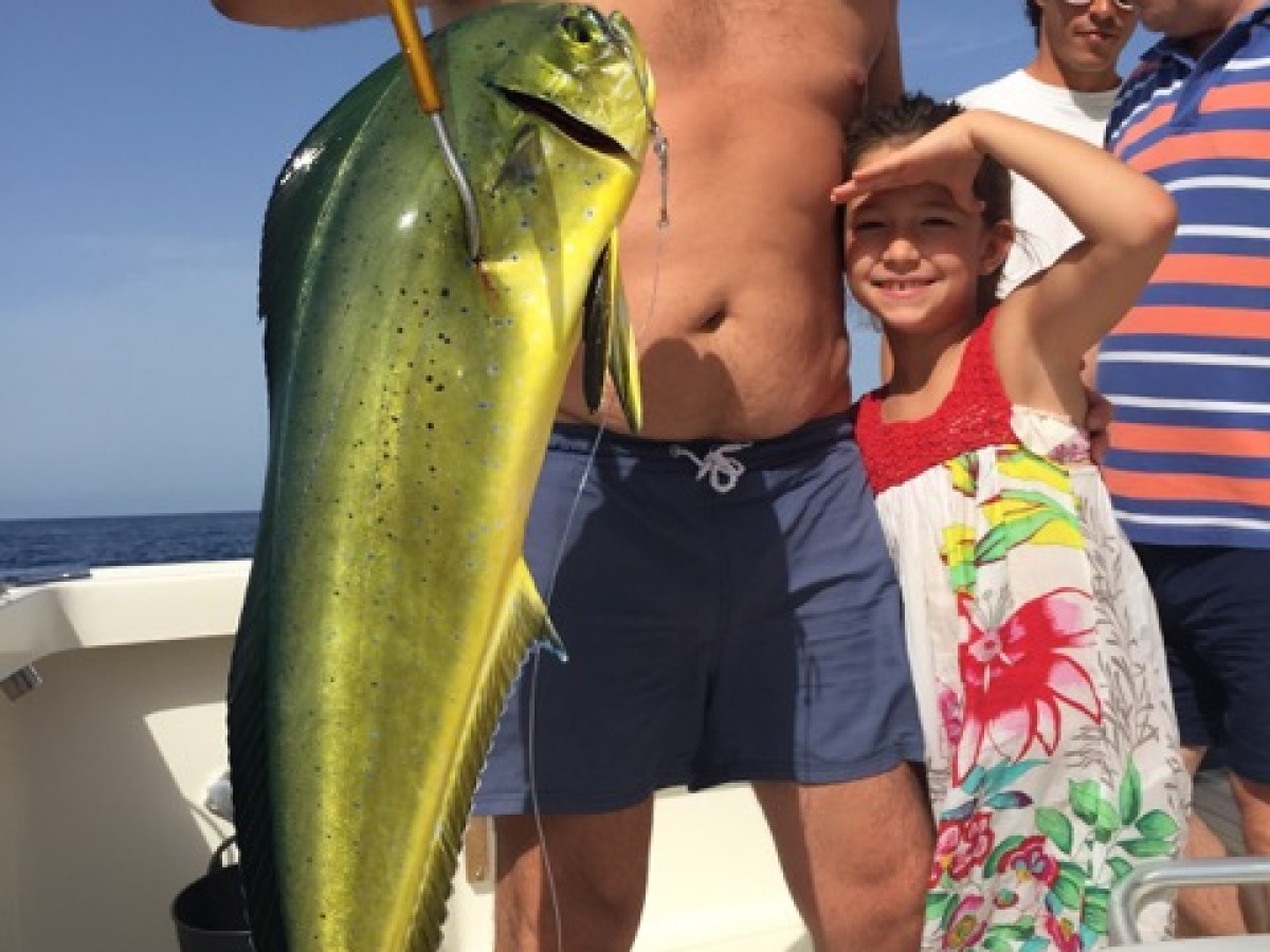 Man and child on a boat holding a large dorado fish, with more people in the background.