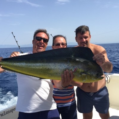 Three men on a boat holding a large fish with the ocean in the background.