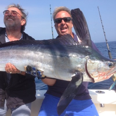 Two men on a boat holding a large fish with fishing rods in the background.