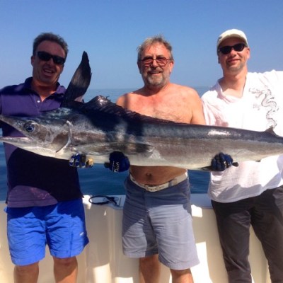 Three men on a boat holding a large marlin with the ocean in the background.