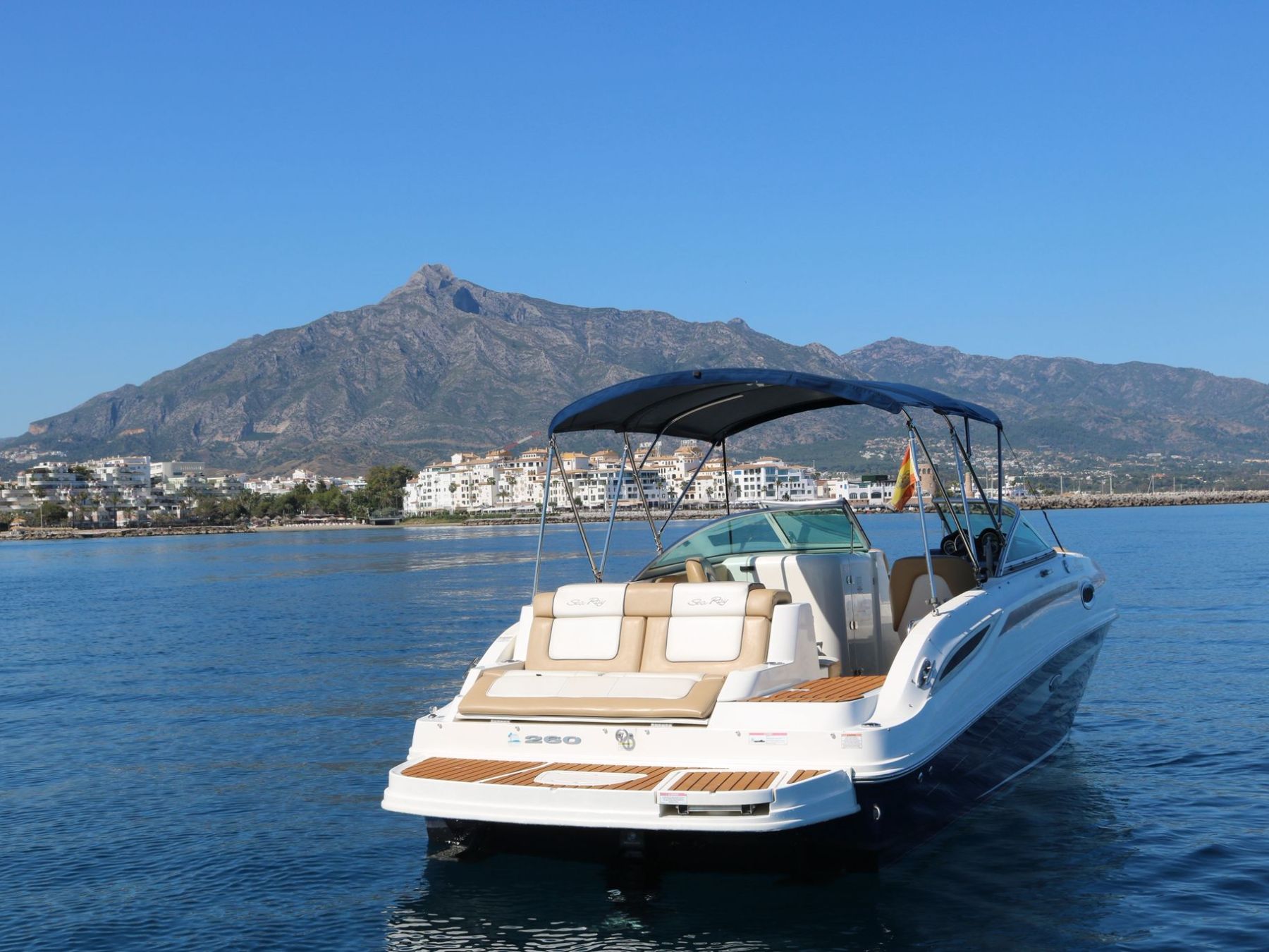 A motorboat on calm water with mountains and buildings in the background.