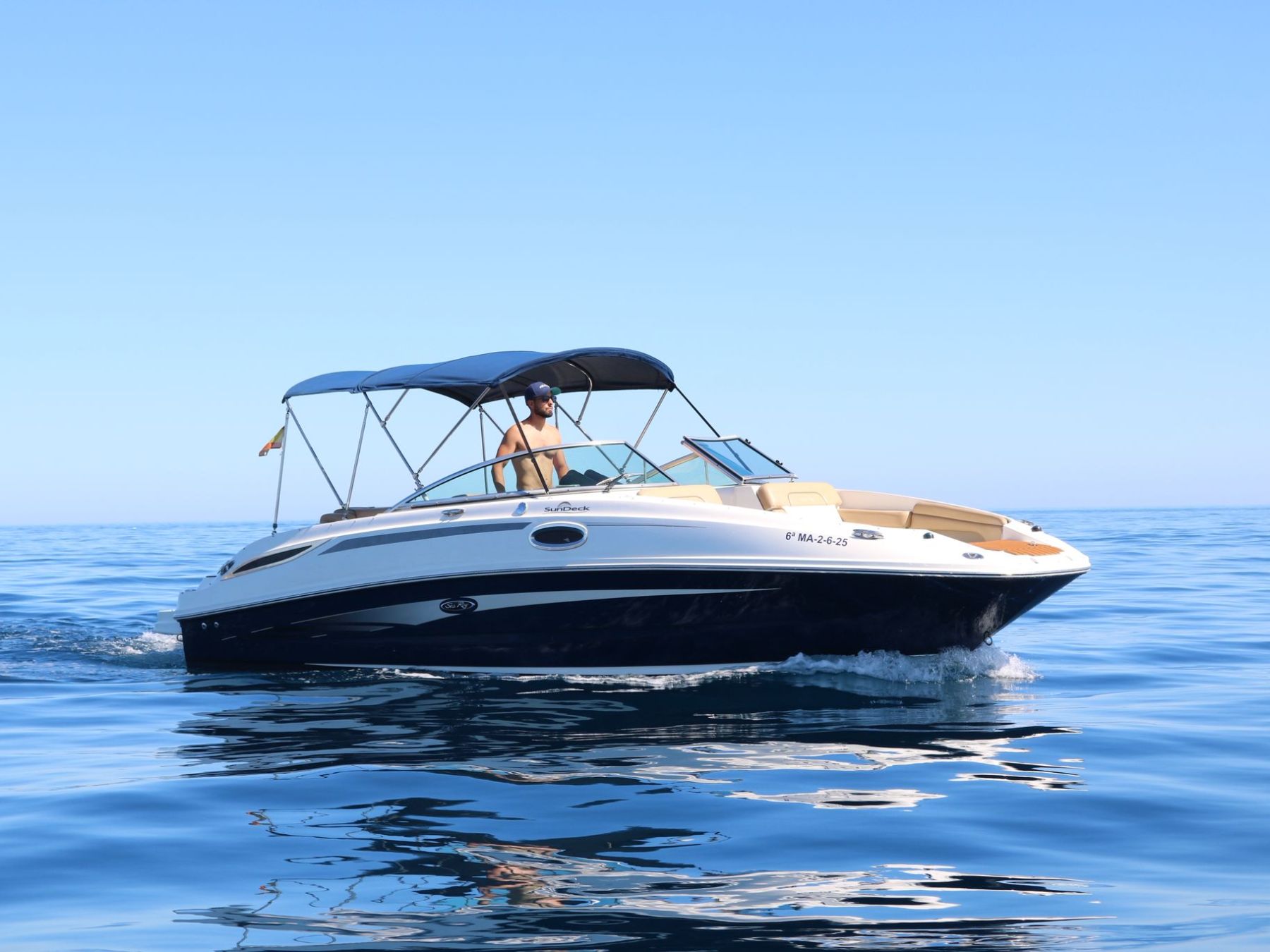 A motorboat with a canopy cruising on calm blue water under a clear sky.