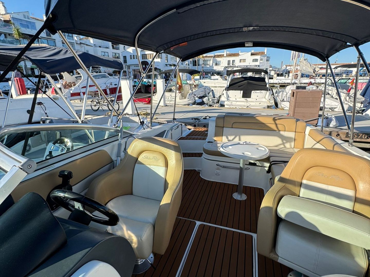 Interior of a motorboat with navy canopy, beige seats, and wooden deck in a marina.