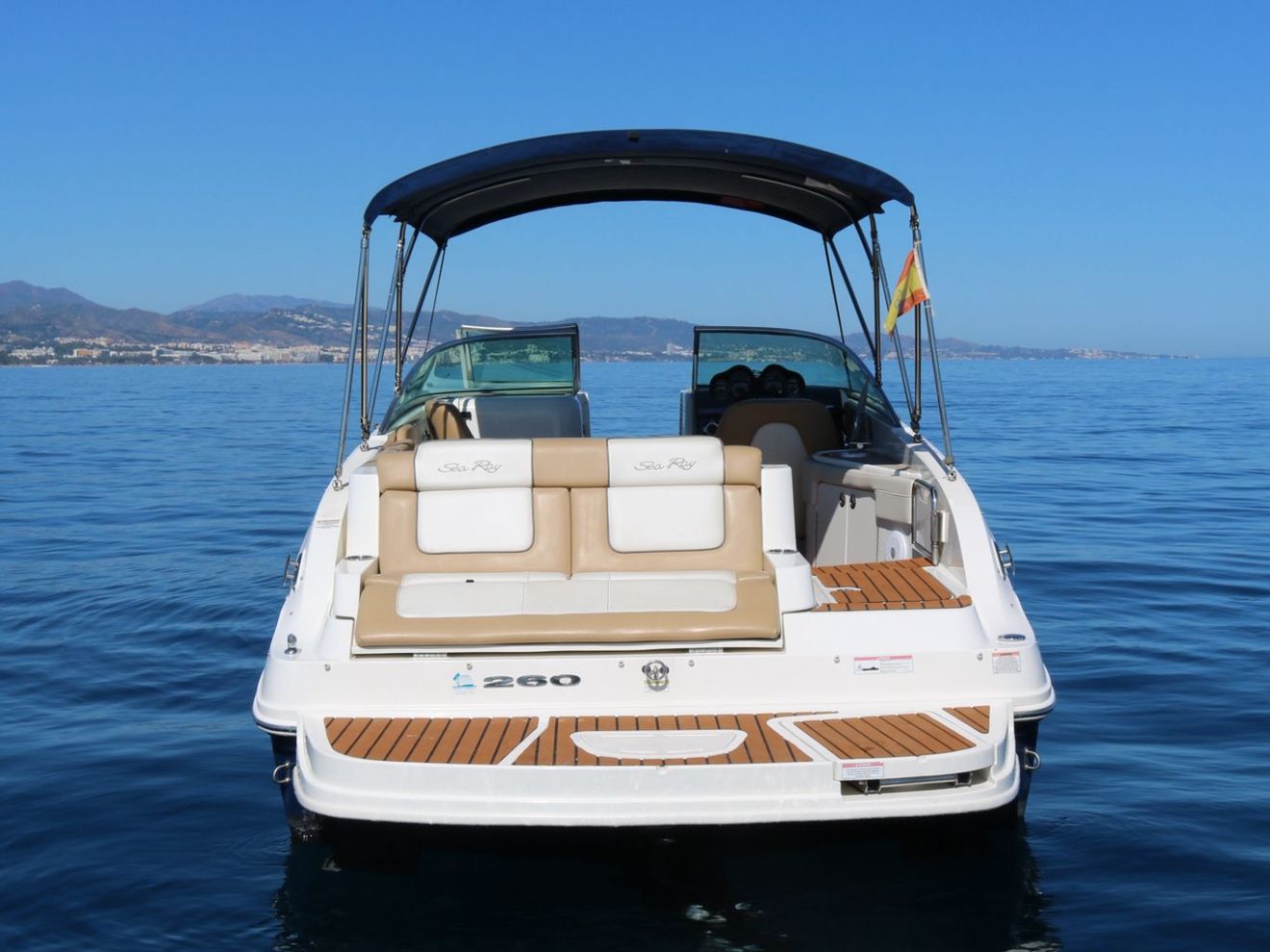 Back view of a motorboat on calm water with clear blue sky.