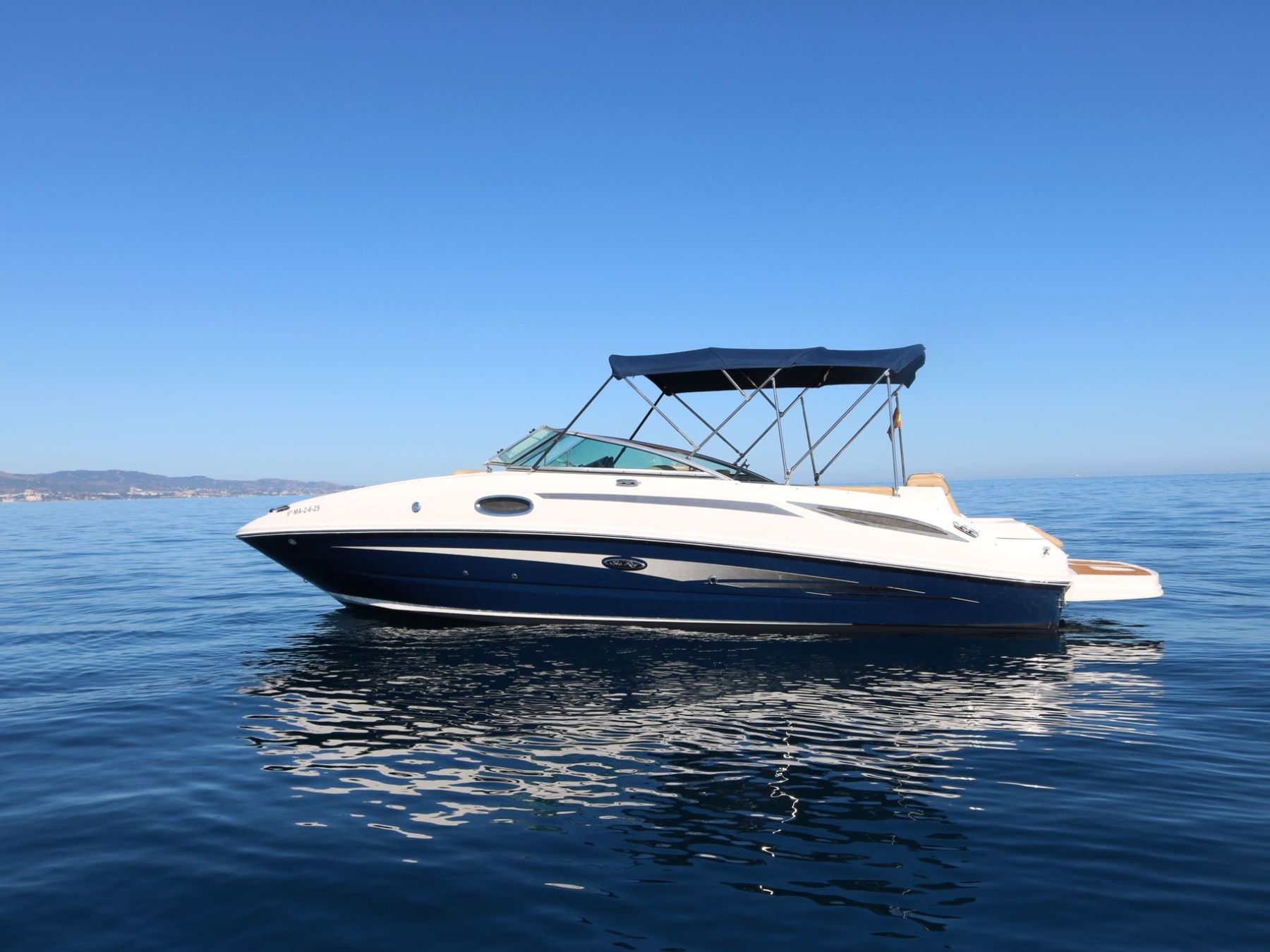 Motorboat with blue canopy on calm sea under clear blue sky.