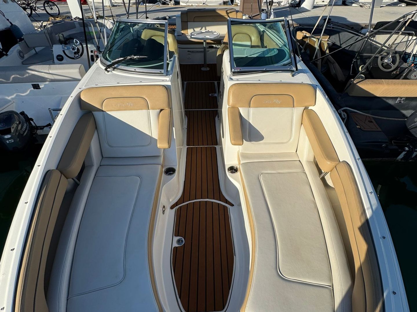 View of a docked boat with tan cushioned seats and wooden flooring in a marina.