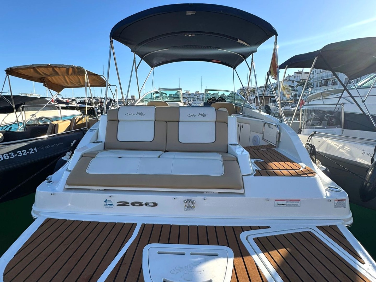 A docked motorboat with a wooden deck and blue canopy under clear sky at a marina.