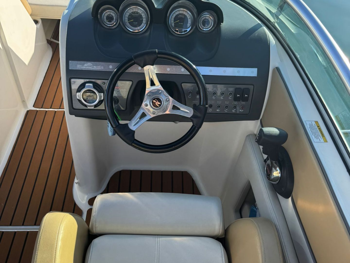 Steering wheel and dashboard of a motorboat with beige leather seat and wood flooring.