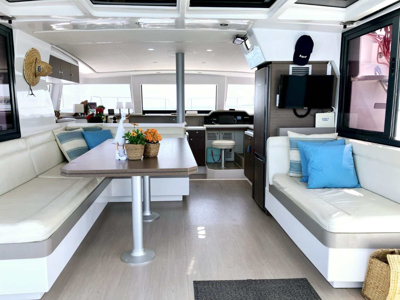 Boat interior with sofa seating, table with plants, and helm station visible.