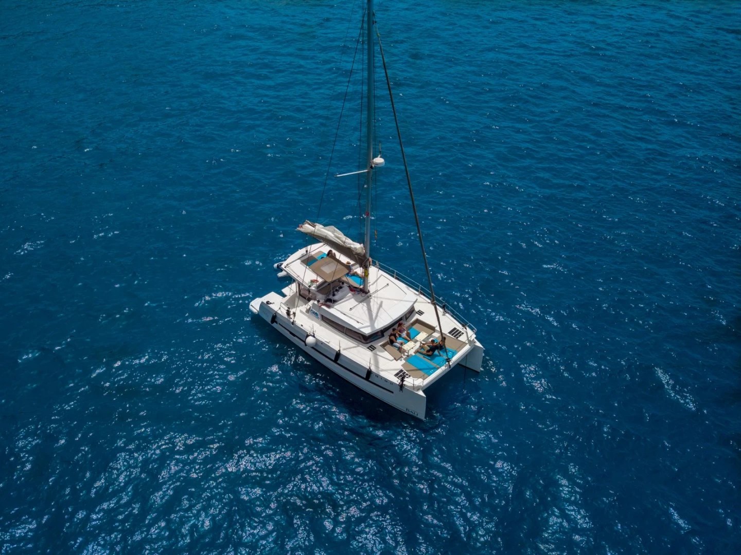 Aerial view of a catamaran sailing in clear blue ocean waters.