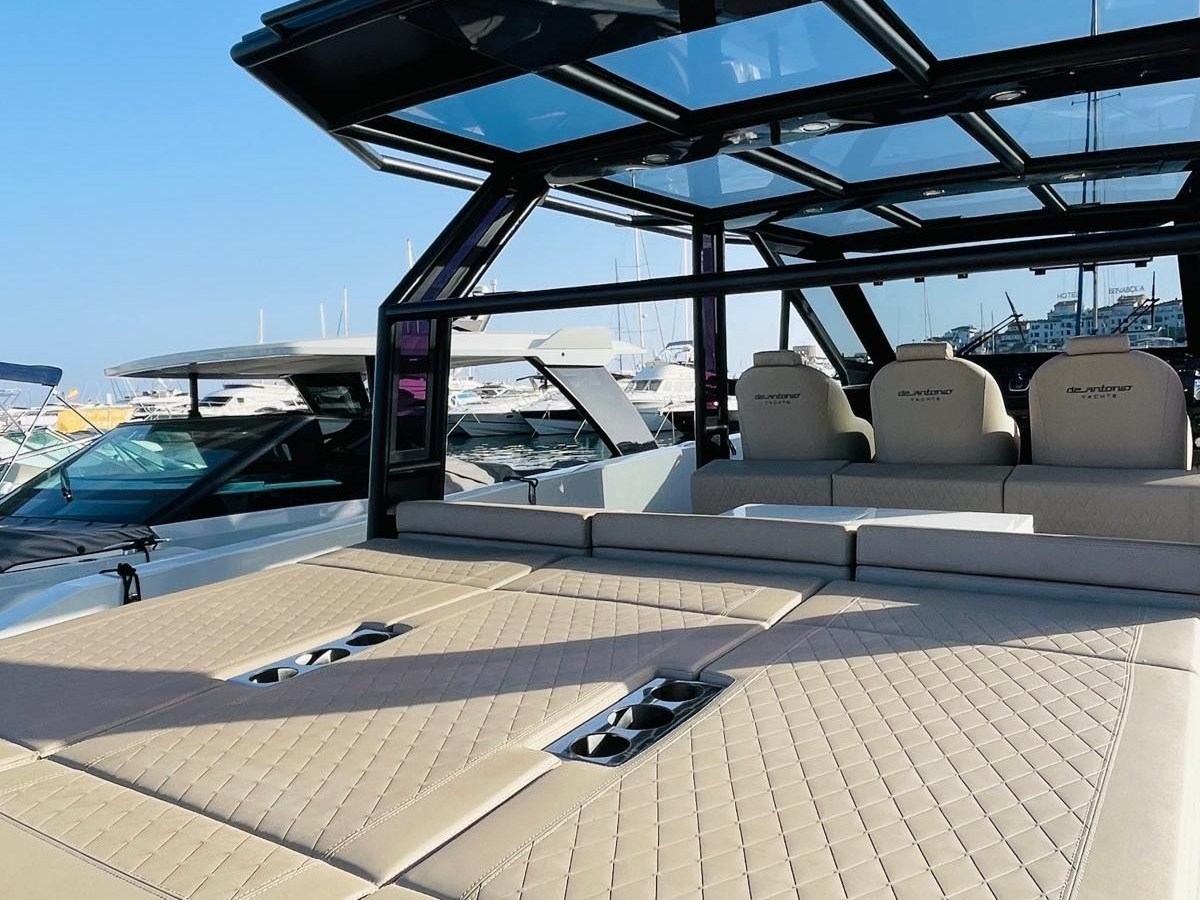 Luxurious boat with beige cushioned seating, glass canopy, and flag on a clear day at a marina.