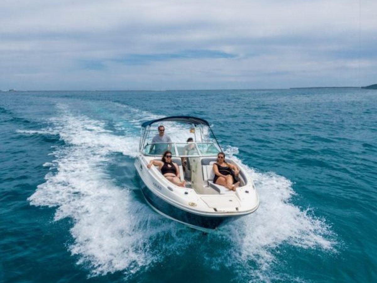 Motorboat with three people cruising on calm blue sea under cloudy sky.