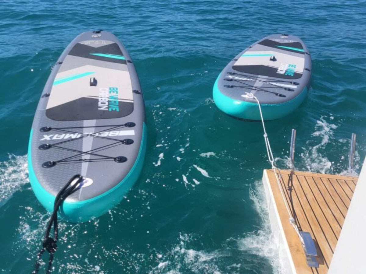 Two paddleboards tethered to a boat on clear blue water.