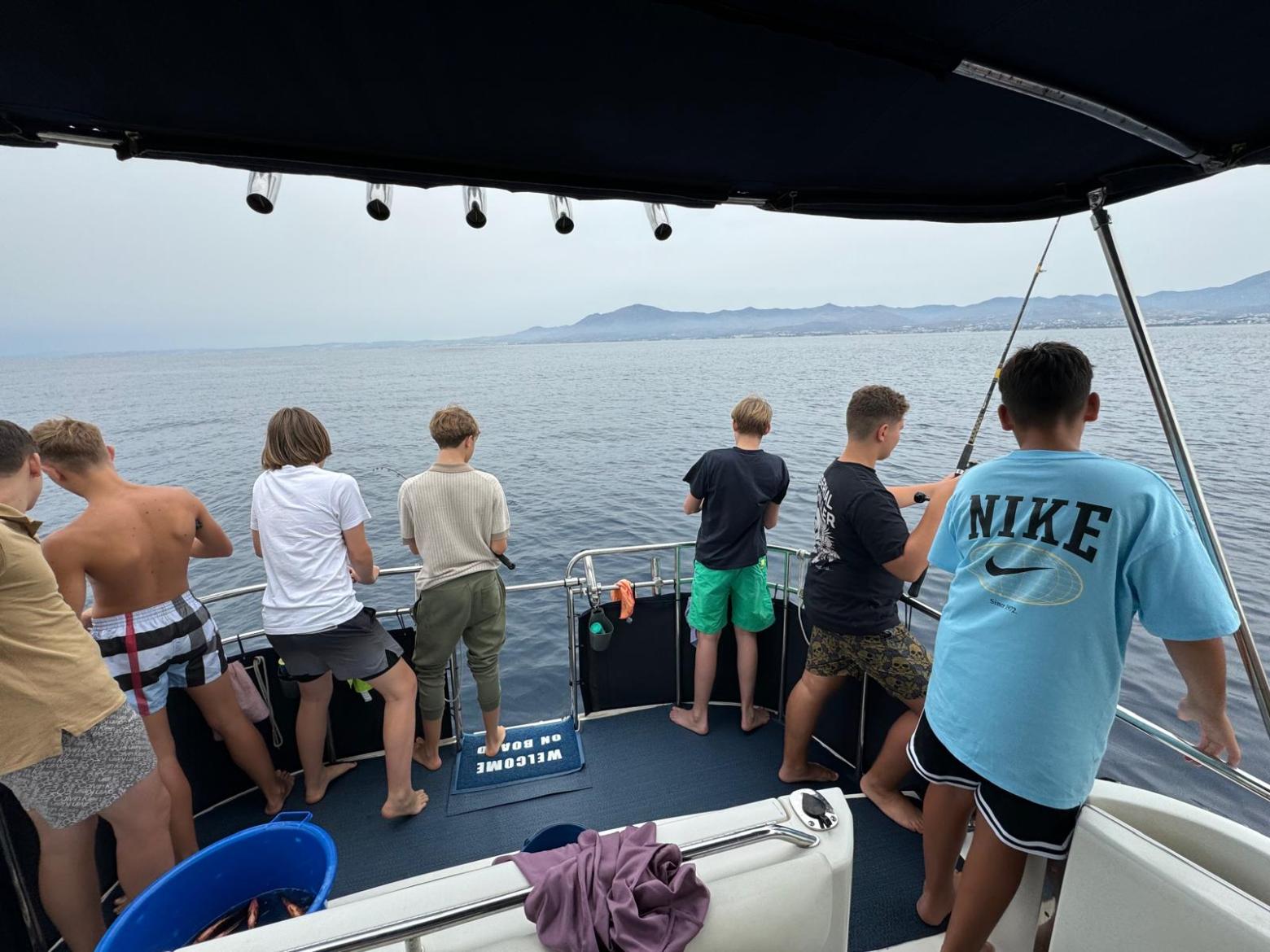 People fishing from a boat, overlooking calm sea with distant mountains.