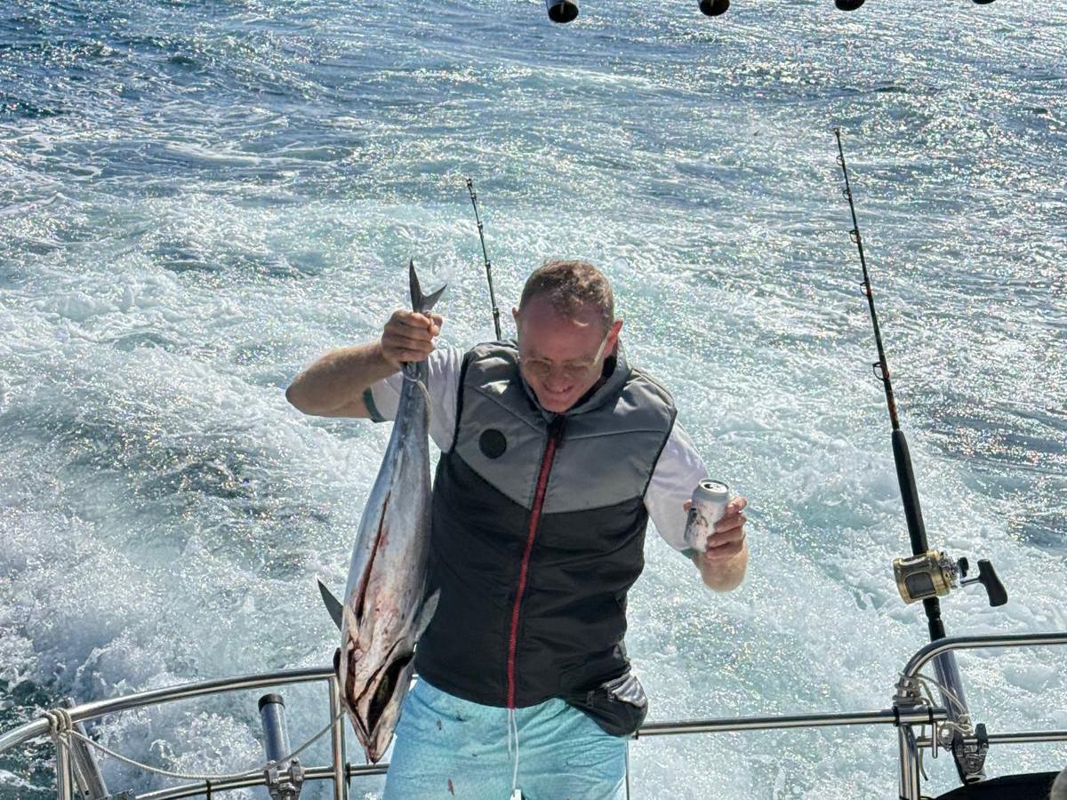 Person on a boat holding a caught fish and a drink with a fishing rod nearby.
