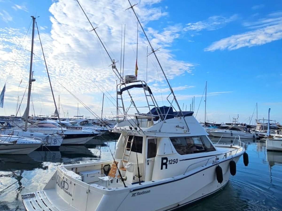 A white boat with antennas docked in a marina under a blue sky with scattered clouds.