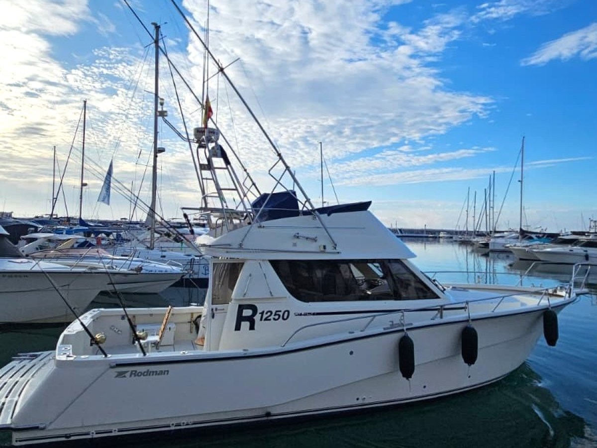 White motorboat docked at a marina under a cloudy blue sky.