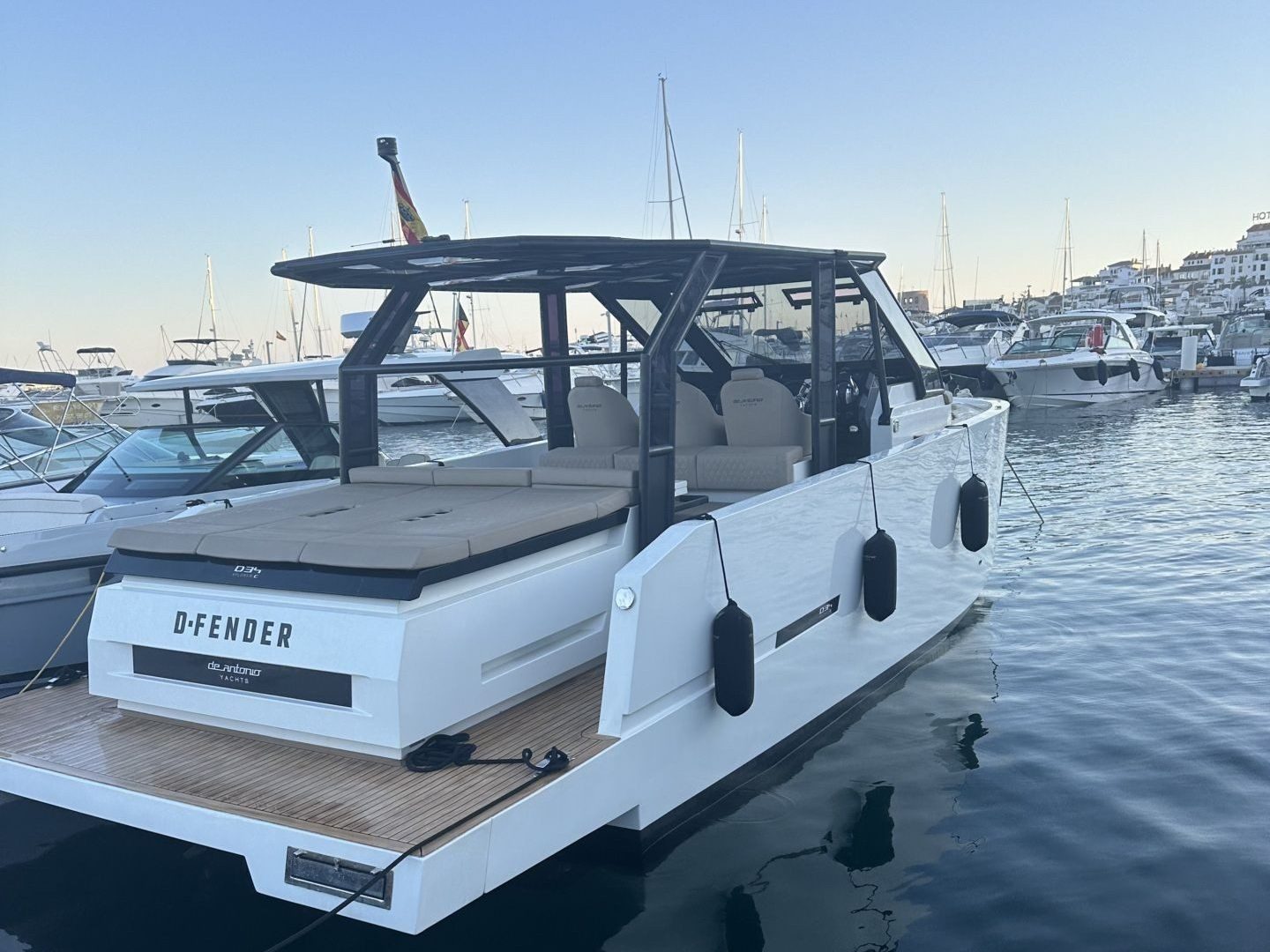Modern white motor yacht docked at a marina with other boats visible in the background.